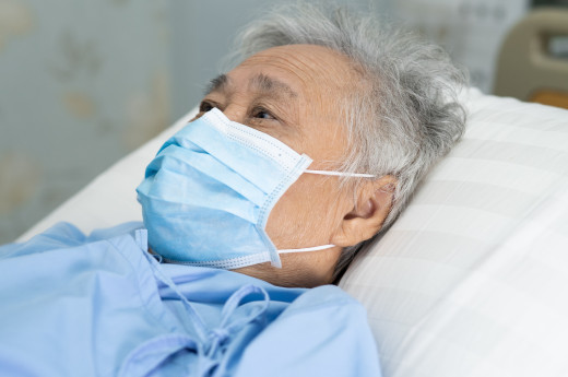 An old man lying on bed, wearing surgical mask