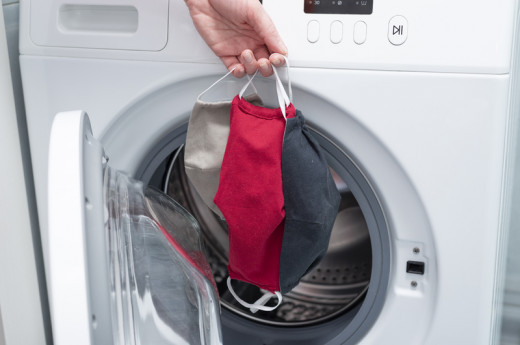 A hand putting clothes masks in a washing machine
